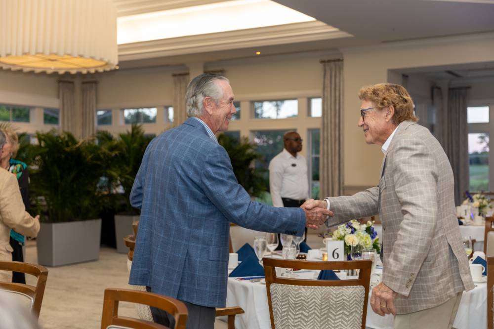 Two gentleman at event smiling and shaking hands